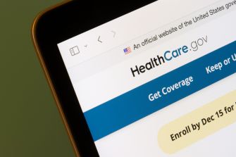 Close-up of a smartphone displaying the HealthCare.gov Marketplace website and “Get coverage” enrollment prompt.