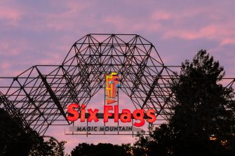 Six Flags Magic Mountain entrance sign beneath the park’s roller-coaster structure at sunset.