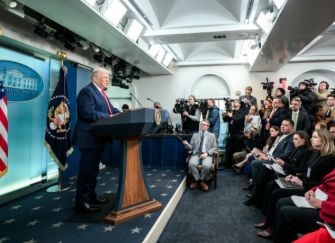 President Donald Trump speaks at a White House press briefing as reporters and photographers watch.