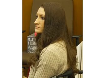 Lindsay Clancy sits in a courtroom, shown in profile with long brown hair and wearing a beige sweater.