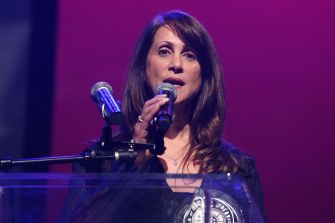 Robin Kaye sings into a microphone onstage under purple lighting.