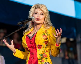 Dolly Parton performs onstage in a bright yellow floral suit while singing into a microphone.
