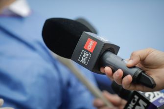 Microphone held toward a masked journalist during a press interview.