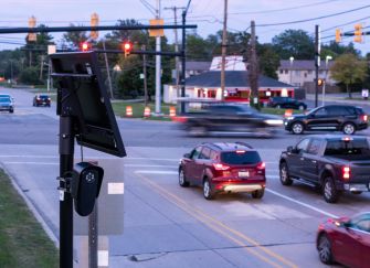 An automated license plate reader stands beside a busy intersection as vehicles pass through the area.