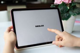 Hands point toward a tablet displaying the Roblox logo.