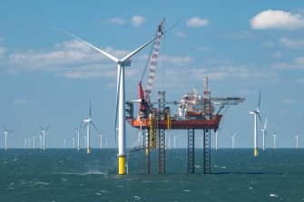 Offshore wind turbines and a construction platform stand in the ocean under a partly cloudy sky.