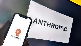Smartphone displaying the Anthropic logo in front of a printed Anthropic sign.