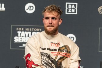 Jake Paul sits in front of a promotional backdrop at a press event.
