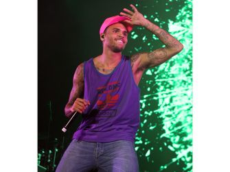 Chris Brown performs onstage in a purple tank top, holding a microphone and raising one hand.