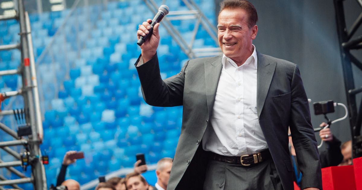 Photo: lawcommentary.com Arnold Schwarzenegger holds a microphone while standing onstage before a crowd