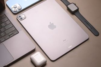 Apple iPhone, iPad, Apple Watch, and AirPods arranged beside a laptop, illustrating the devices affected by the haptic technology patent verdict.