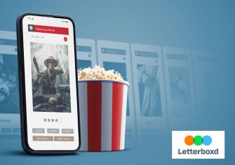 Smartphone displaying a movie review app beside a tub of popcorn, with film listings and the Letterboxd logo in the background.