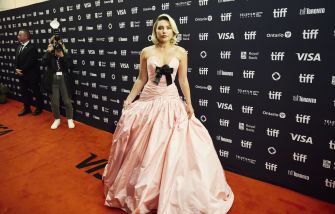 Florence Pugh poses on a red carpet in a pale pink gown before a sponsor-branded backdrop.