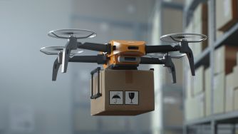 Drone carrying a cardboard package flies through a warehouse aisle.