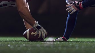 Football players line up on a field, with one player holding the ball as another prepares to kick it.