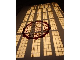 Cornell University seal cast in warm light amid shadows from tall windows.
