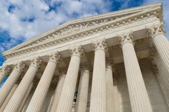 The U.S. Supreme Court building viewed from below against a partly cloudy sky.