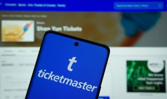 Ticketmaster logo displayed on a smartphone in front of a blurred ticketing website.