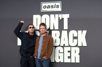 Noel and Liam Gallagher pose in front of a large Oasis “Don’t Look Back in Anger” display.