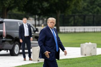 Donald Trump walks across a lawn near a parked SUV and a security aide.