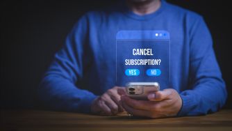 Person in a blue shirt taps a smartphone displaying a “Cancel subscription?” prompt with yes and no options.