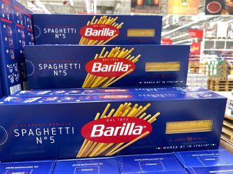 Stacked blue boxes of Barilla spaghetti pasta displayed in a supermarket aisle.