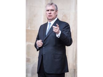 Andrew Mountbatten-Windsor gestures while wearing a dark suit outside a building.