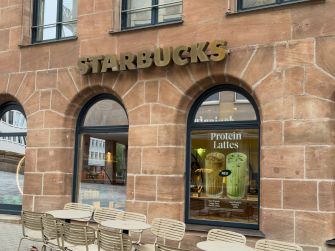 Starbucks storefront with outdoor seating and a window display advertising protein lattes.