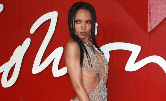 FKA Twigs poses in a silver chainmail dress against a red backdrop.