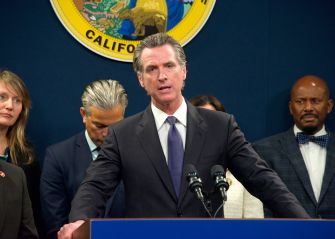 California Gov. Gavin Newsom speaks at a podium during a press conference, with officials standing behind him.