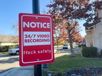 Flock Safety sign warning of 24/7 video recording on a residential street.