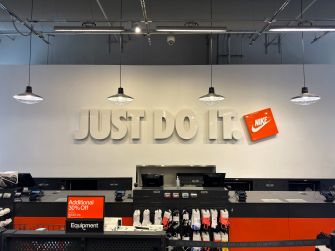 Nike store interior with “JUST DO IT” wall branding, Nike logo, and retail counters displaying sports equipment and apparel.