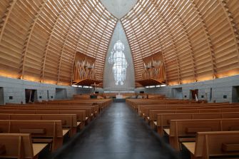 Interior of a Catholic church with rows of wooden pews, a central aisle, and a large crucifix beneath a vaulted wooden ceiling.
