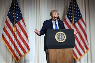 Donald Trump speaks at a presidential podium between two American flags.