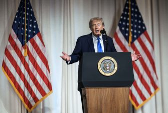 Donald Trump speaks at a podium between two American flags.