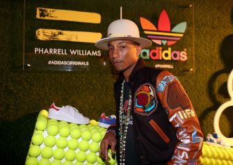 Pharrell Williams poses at an Adidas event beside a display of tennis balls and sneakers.