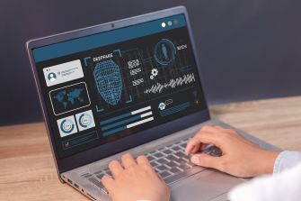 Person using a laptop displaying a deepfake analysis interface with a digital face, maps, charts and audio waveform.