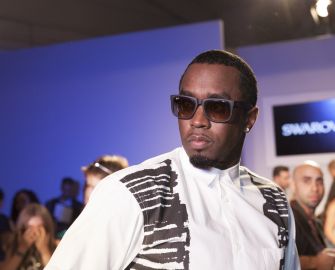 Sean “Diddy” Combs wears sunglasses and a white shirt with a black patterned vest at a public event.