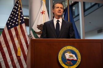 California Gov. Gavin Newsom speaks at a podium in front of U.S. and California flags.