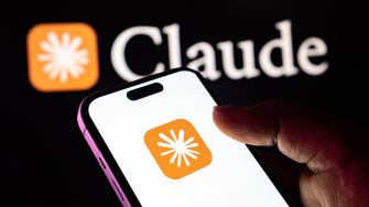 Hand holding a smartphone displaying the Claude logo, with a large Claude logo in the background.