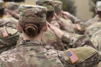 Female U.S. service member salutes while standing among soldiers in formation.