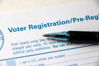 Close-up of a pen resting on a voter registration form with the heading “Voter Registration/Pre-Registration.”