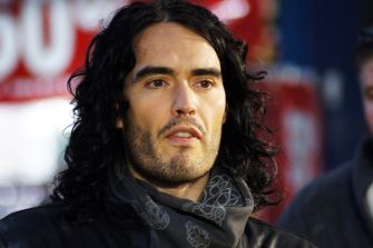 Russell Brand with long dark hair and a patterned scarf at a public event.