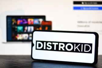 DistroKid logo displayed on a smartphone in front of blurred music streaming screens.