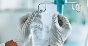 Gloved medical professional holds an intravenous drug infusion bag in a clinical setting.
