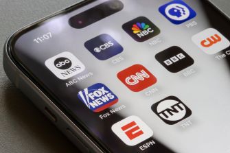 Smartphone displaying apps for ABC News, CBS, NBC, CNN, Fox News, BBC, PBS, The CW, TNT and ESPN.