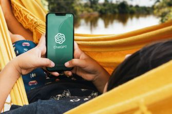 Person seated in a hammock holds a smartphone displaying the ChatGPT logo.
