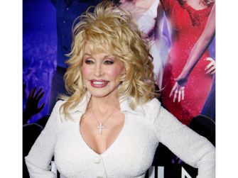 Dolly Parton smiles while posing at a public event in a white outfit.