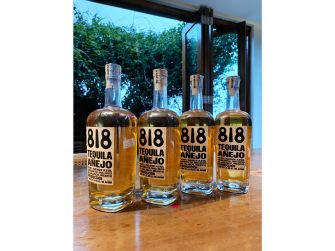 Four bottles of 818 Tequila, including Blanco, Reposado, and Añejo varieties, displayed on a wooden table.