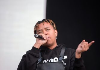 Rapper Cordae performs onstage, holding a microphone and gesturing with his other hand.